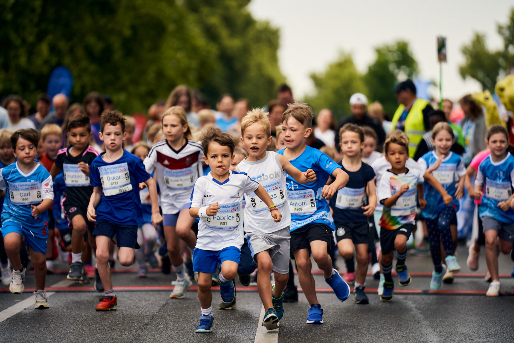 Kinder beim Start eines Laufwettbewerbs, voller Energie und Begeisterung, mit Teilnehmern in bunten Sportoutfits und Nummern auf der Brust.