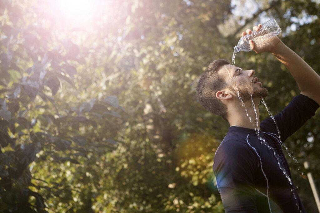 Mann erfrischt sich mit Wasserflasche im Freien, Sonnenschein und grüne Umgebung.