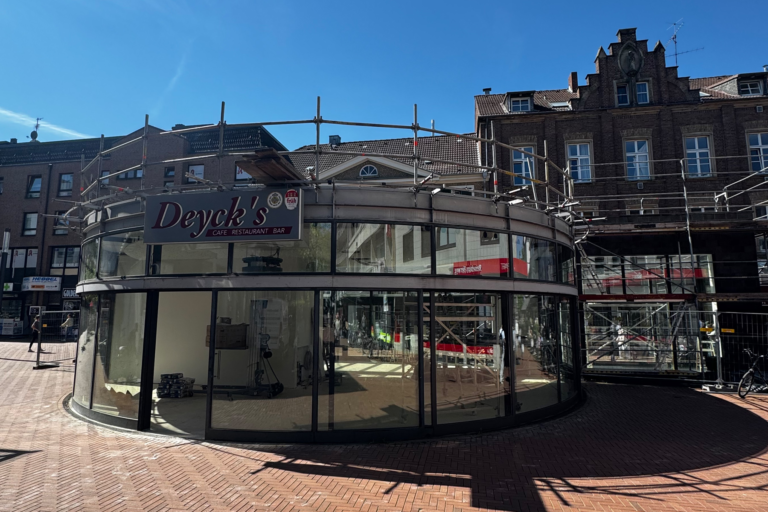 Deyck's Café Restaurant Bar im Bau, moderne Glasfassade mit Gerüst in belebter Innenstadt.