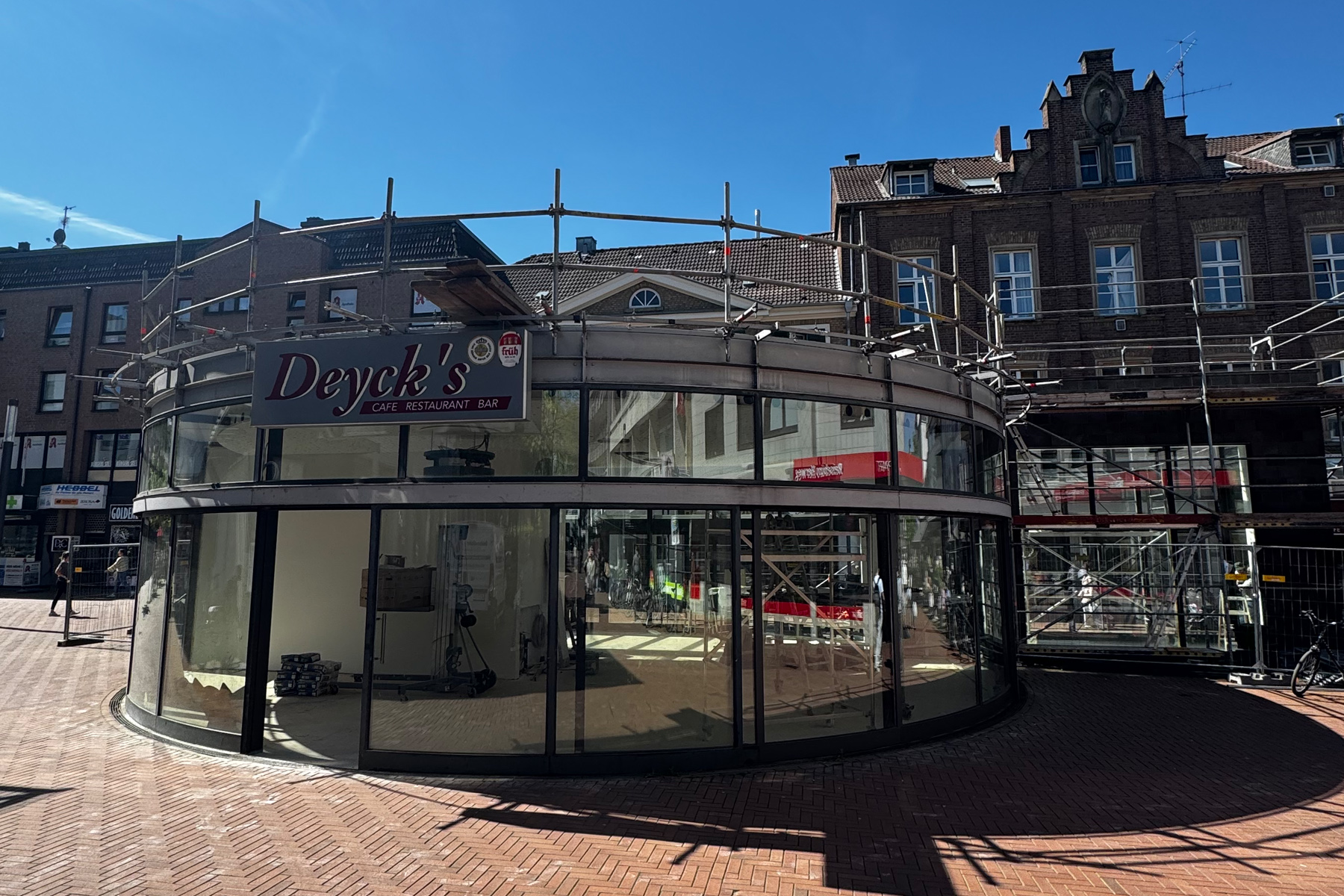 Deyck's Café Restaurant Bar im Bau, moderne Glasfassade mit Gerüst in belebter Innenstadt.