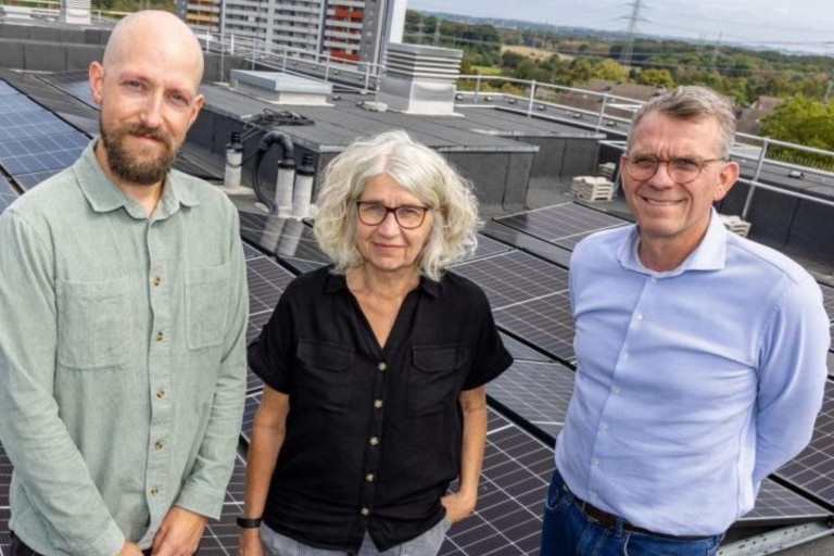 Drei Personen stehen auf einem Dach mit Solarpanelen, im Hintergrund eine grüne Landschaft. Das Bild illustriert das neue PV-Mieterstrom-Projekt der WGL und EVL.
