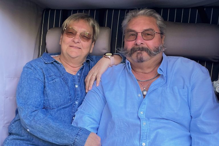 A smiling couple in blue shirts is sitting comfortably on a couch, enjoying their time together.